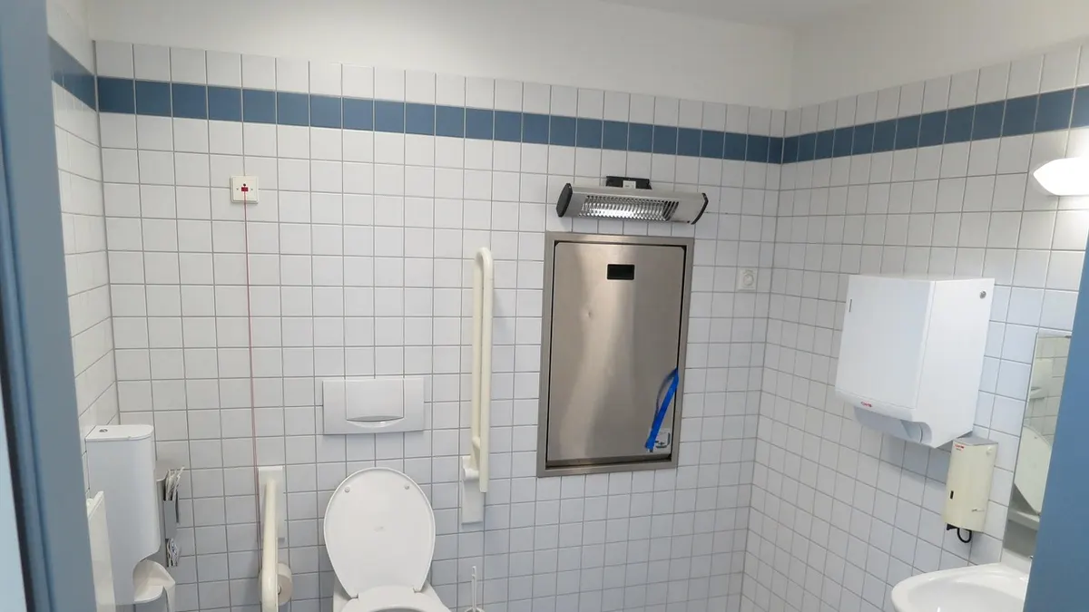 Vaso sanitário em banheiro azulejado com pia ao fundo