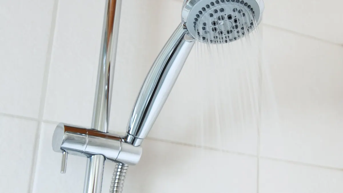 Ducha cromada com água caindo em banheiro de azulejos brancos