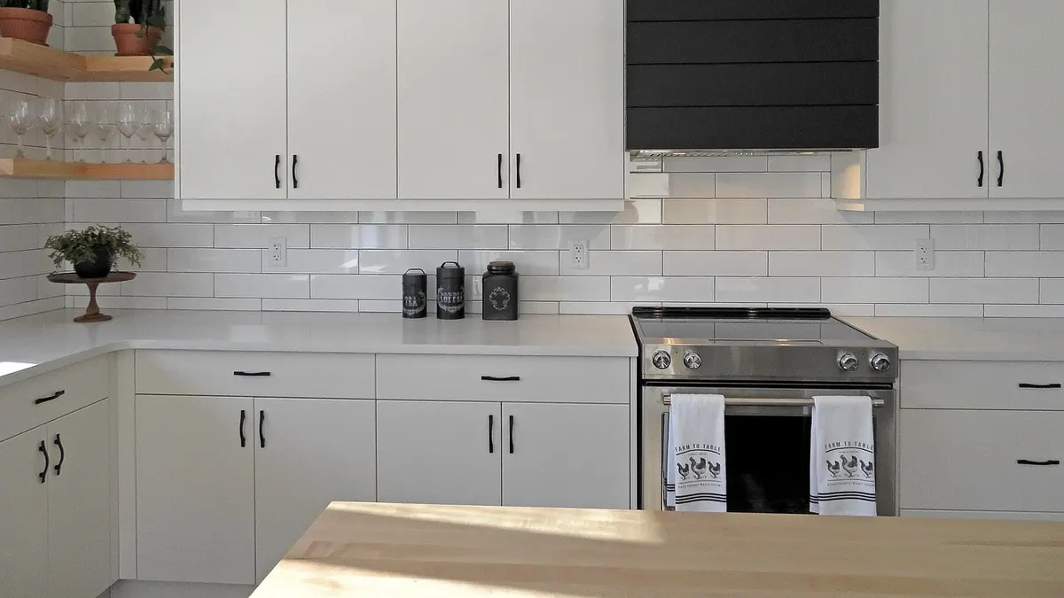 Cozinha branca clara com armários, fogão e azulejos de metrô