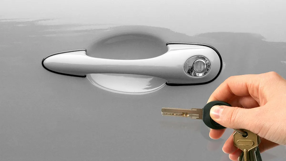 Mão inserindo chave na maçaneta de um carro prateado